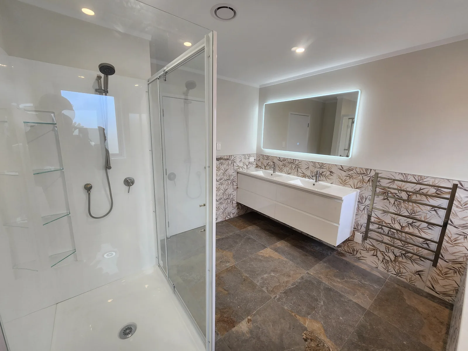 Walk-in shower and double vanity against a botanical feature-tile wall in a Massey bathroom, West Auckland, tiled by Tarara Tiling
