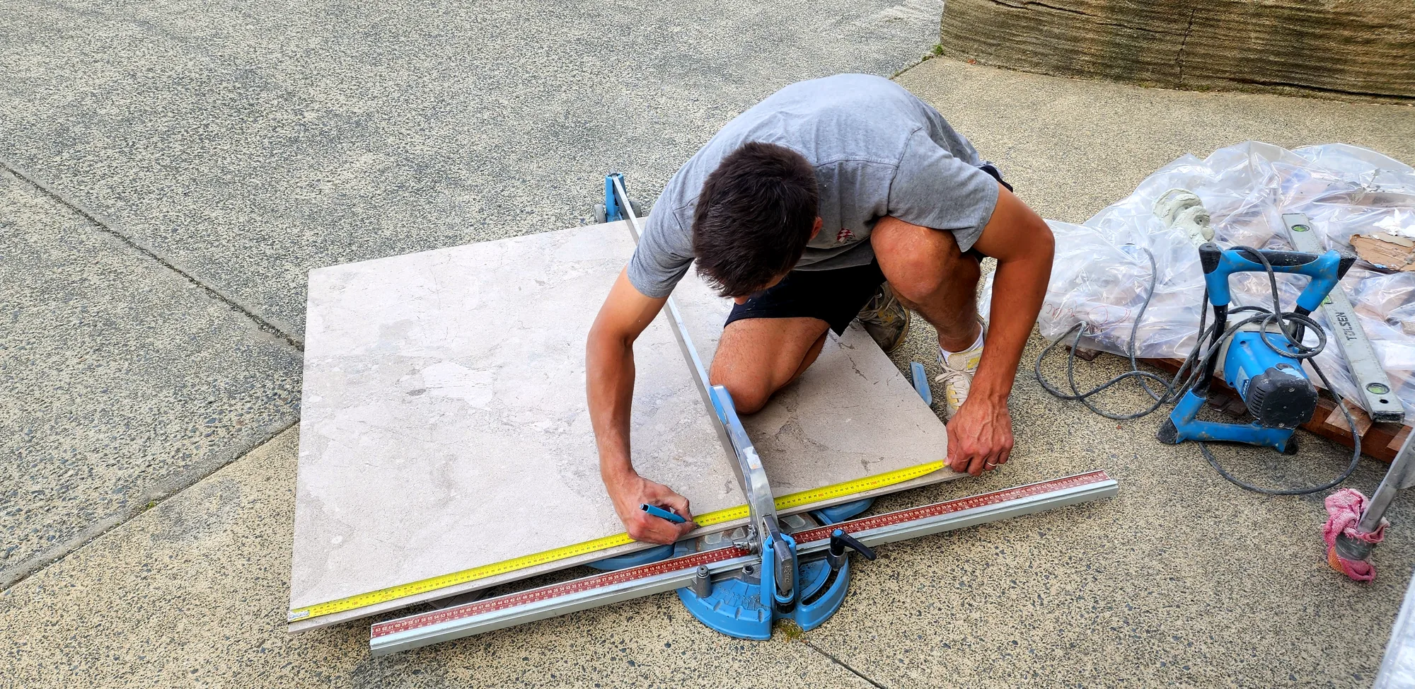 Marko scoring a large-format porcelain tile on a rail cutter, Auckland