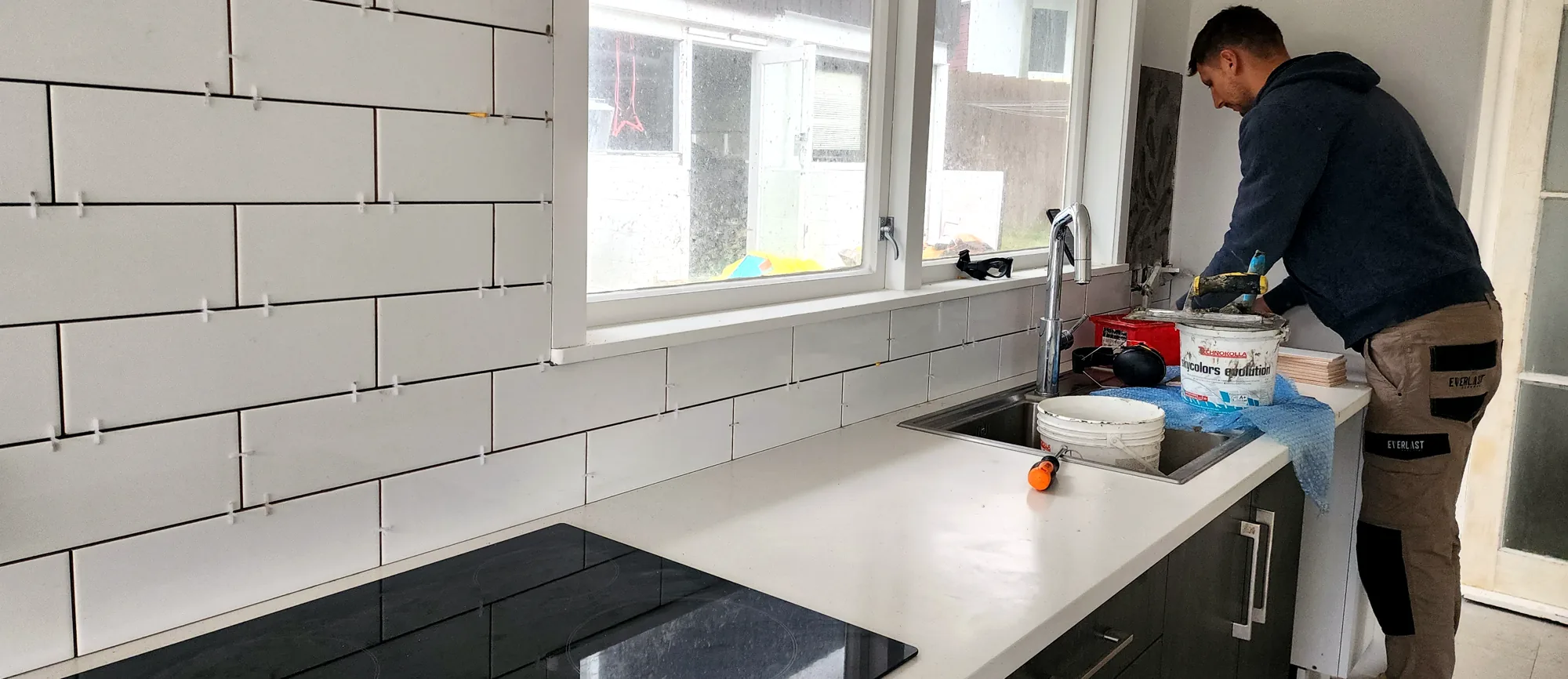 Marko tiling a white brick-bond kitchen splashback in Auckland