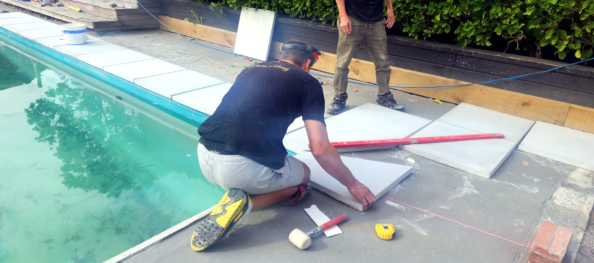 Marko laying a large-format porcelain tile beside a pool in Auckland