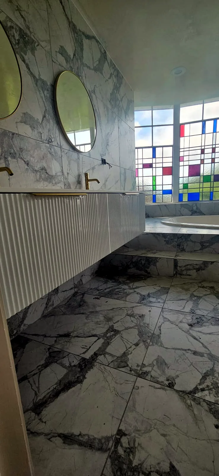 Floor-to-ceiling marble-look tiling with a fluted vanity, brass tapware and leadlight windows in an Auckland bathroom — by Tarara Tiling