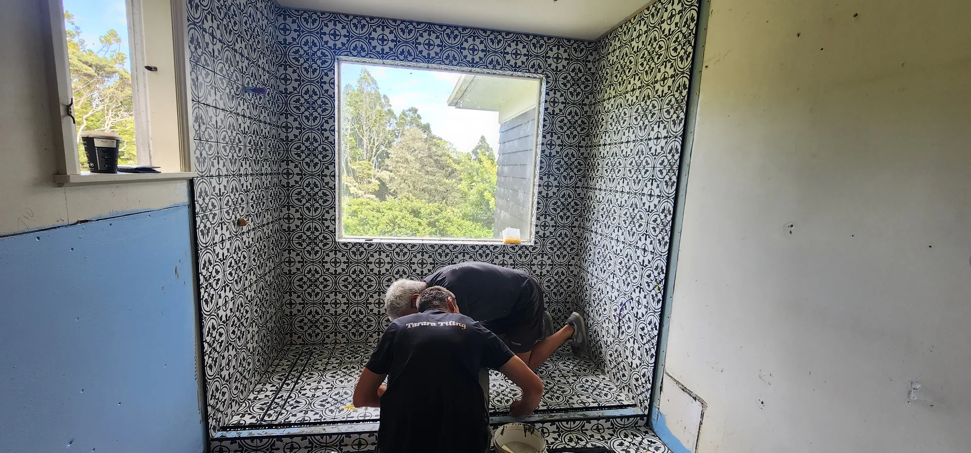Two Tarara Tiling tilers laying a blue-and-white patterned feature bathroom floor in Auckland