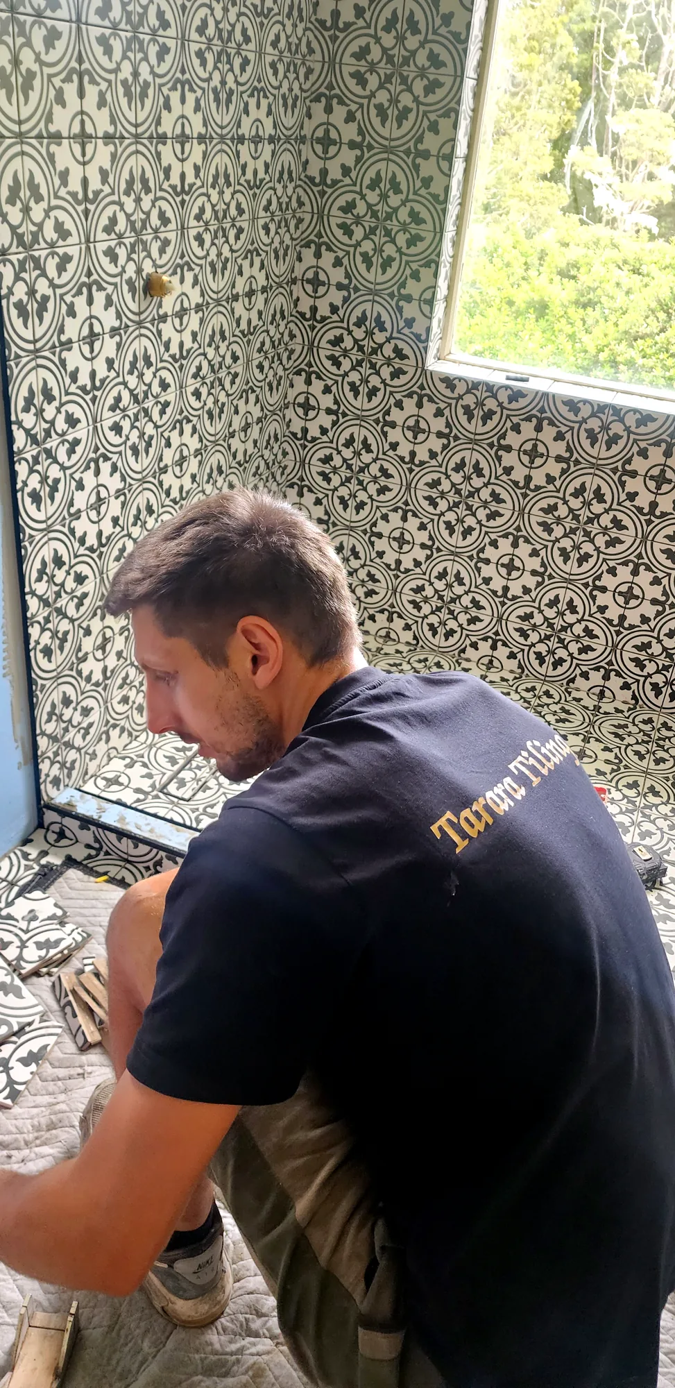 Marko in a Tarara Tiling shirt laying patterned floor tiles in an Auckland bathroom